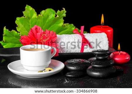beautiful spa concept of red hibiscus flower with dew, candles, green leaf, cup of tea and rolled towel on zen stones