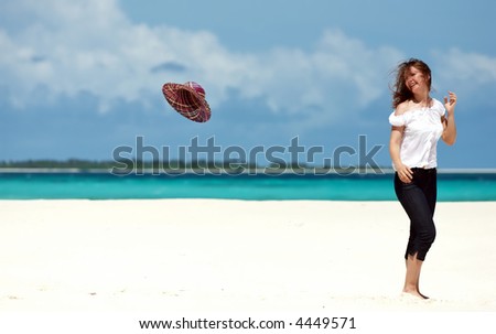 Happy girl on white sand beach looking to flying hat and smiling
