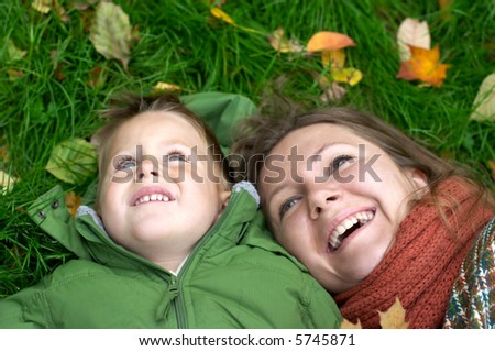 Smiling mother and son on the grass covered with fallen leaves