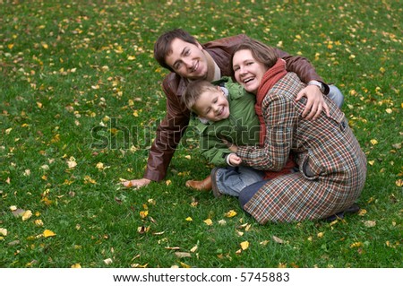 Happy family of three on the grass covered with fallen leaves