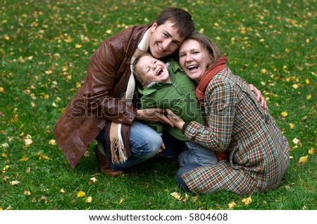 Happy family of three on the grass covered with fallen leaves