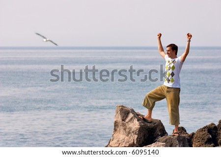 Freedom. Happy young man standing on top of mountain with ocean on background