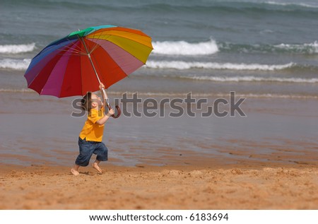Do not depend on weather conditions. Cute small boy with big brightly colored umbrella having fun on the beach