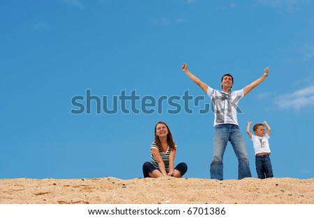 Happy young family of three on top of sand dune with blue-blue sky on background
