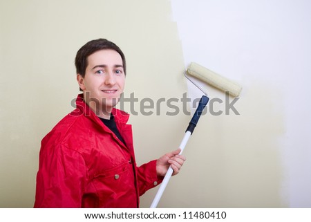 Man painting a wall. Painter in red overall painting wall in light green color