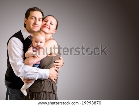 Studio picture of happy young parents and 4 months old baby girl over dark gray background