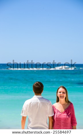 Young happy couple laughing. Man back turned to camera. Turquoise ocean on background.