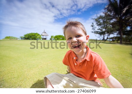 Happy 4 years old boy sitting on green grass at sunny summer day