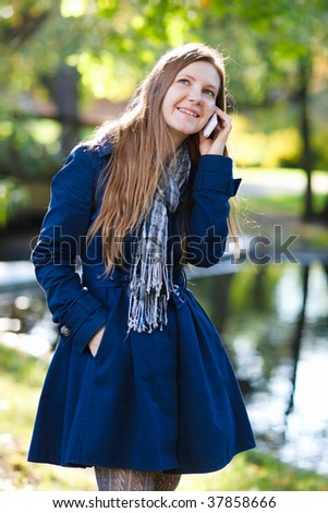 Attractive young woman outdoors at beautiful autumn day talking on mobile phone