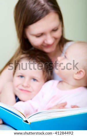 Young mother with her two kids reading book in bed. Focus on book.