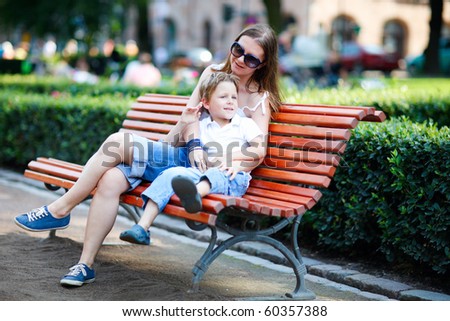 Happy mother and son sitting on bench in city park on summer day
