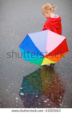 Toddler girl with colorful umbrella, beautiful reflection on wet ground