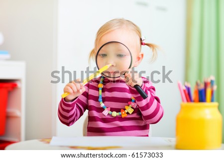 Funny portrait of adorable toddler girl looking through magnifier to a pencil
