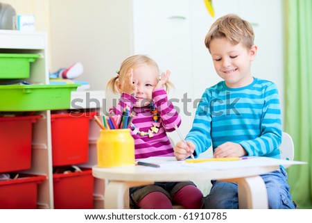 Happy brother and sister sitting together at table and drawing with pencils
