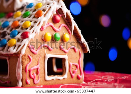 Closeup of gingerbread house decorated with colorful candies over Christmas tree lights background