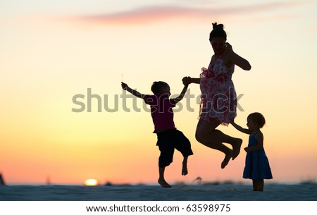 Mother and two kids silhouettes jumping on beach at sunset