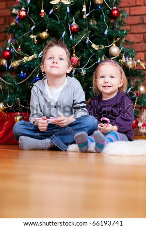 Brother and sister sitting near beautiful Christmas tree