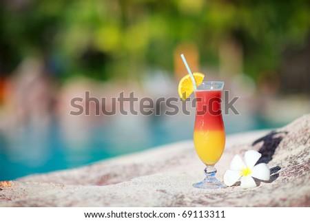 Colorful tropical cocktail and frangipani flower near water