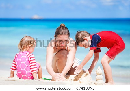 Young mother and her two kids building sand castle at beach