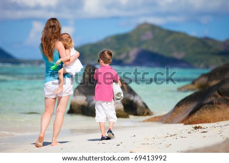 Back view of mother and two small kids walking along tropical beach