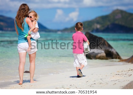 Back view of mother and two small kids walking along tropical beach