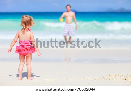 Back view of playful toddler girl on white sand beach with her father