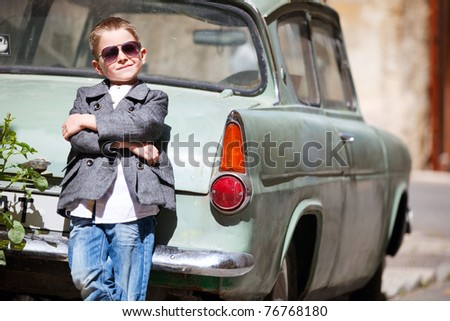 Six years old boy outdoors in citystandimg near old car