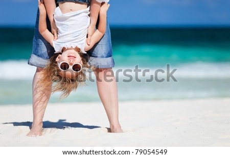 Mother holding her happy smiling daughter upside down having beach fun