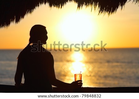 Silhouette of young woman having drink at sunset