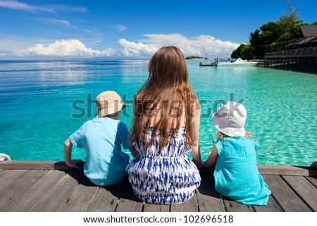 Back view of mother and kids sitting on wooden dock