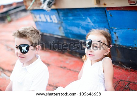 Cute little pirates boy and girl sitting at old boat