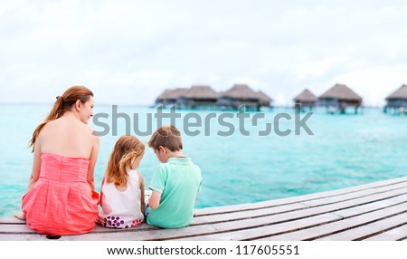 Mother and kids sitting at wooden dock enjoying ocean view