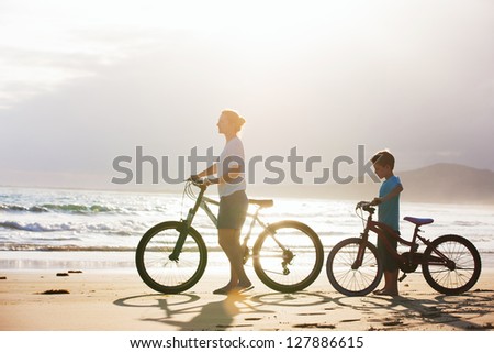 Mother and son with bikes on a beach at sunset