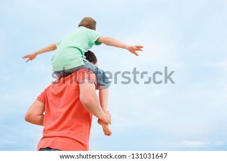 Back View Of Father Carrying His Son On Shoulders