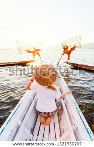 Back view of young woman in a small boat watching Burmese fishermen on bamboo boats catching fish traditional way in lake Inle Myanmar