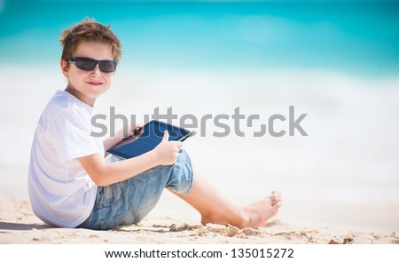 Little boy at beach playing on a tablet device