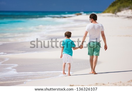 Back view of father and son walking along tropical beach