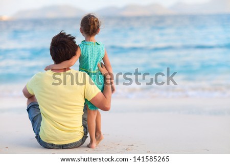 Back view of a father and his sweet little daughter at beach