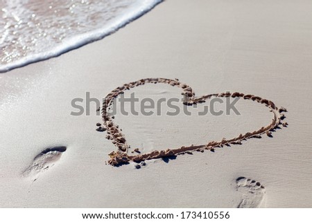 Heart drawn on beach sand and sea wave