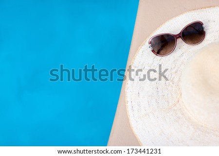 White straw hat and sun glasses by a swimming pool