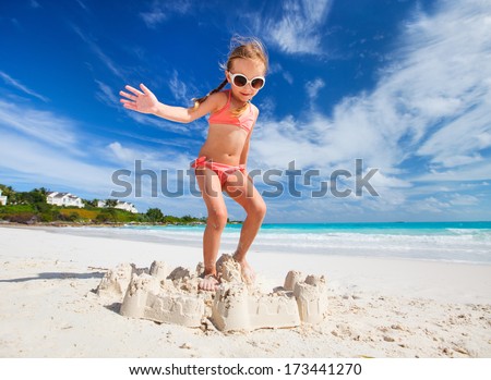Little girl at tropical beach jumping on a sand castle having fun