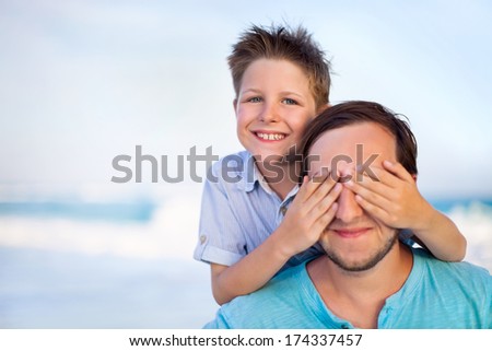 Portrait Of Happy Boy Covering Father\'S Eyes At Beach