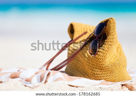 Close up of a straw bag, sun glasses and towel on a tropical beach