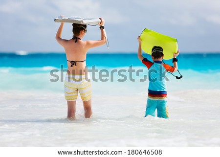 Mother and son running towards ocean with boogie boards