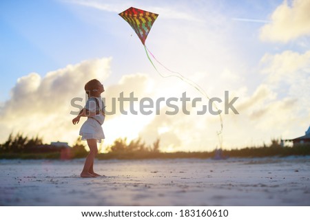 Little girl flying a kite on beach at sunset
