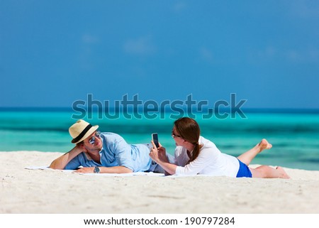 Young couple relaxing on a beach taking photos of each other during tropical vacation