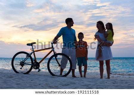 Silhouettes of a family with two kids and a bike on tropical beach at sunset
