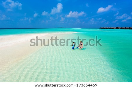 Above view of  mother and son walking at shallow turquoise ocean water with snorkeling equipment