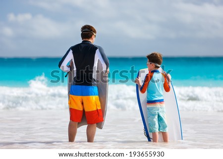 Father and son at beach facing ocean with boogie boards