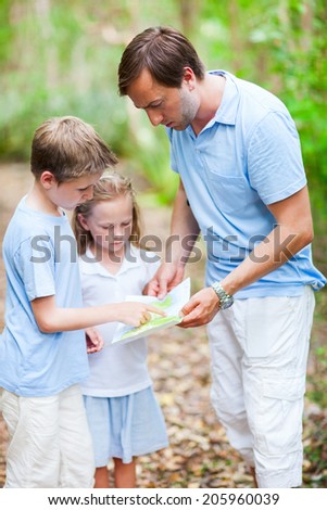 Family of father and little kids looking on map while hiking at forest or park
